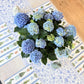 Bouquet of blue hydrangeas on a decorative table runner with a wooden surface.
